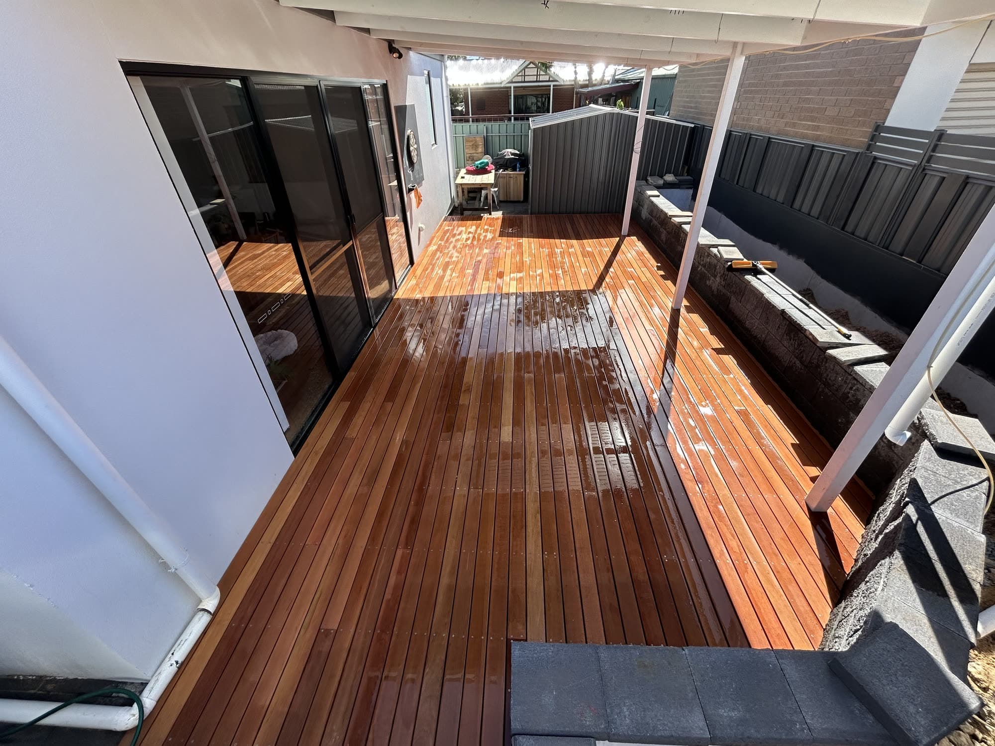 Freshly oiled merbau deck running under a pergola breezeway, with a dark cladding fence behind